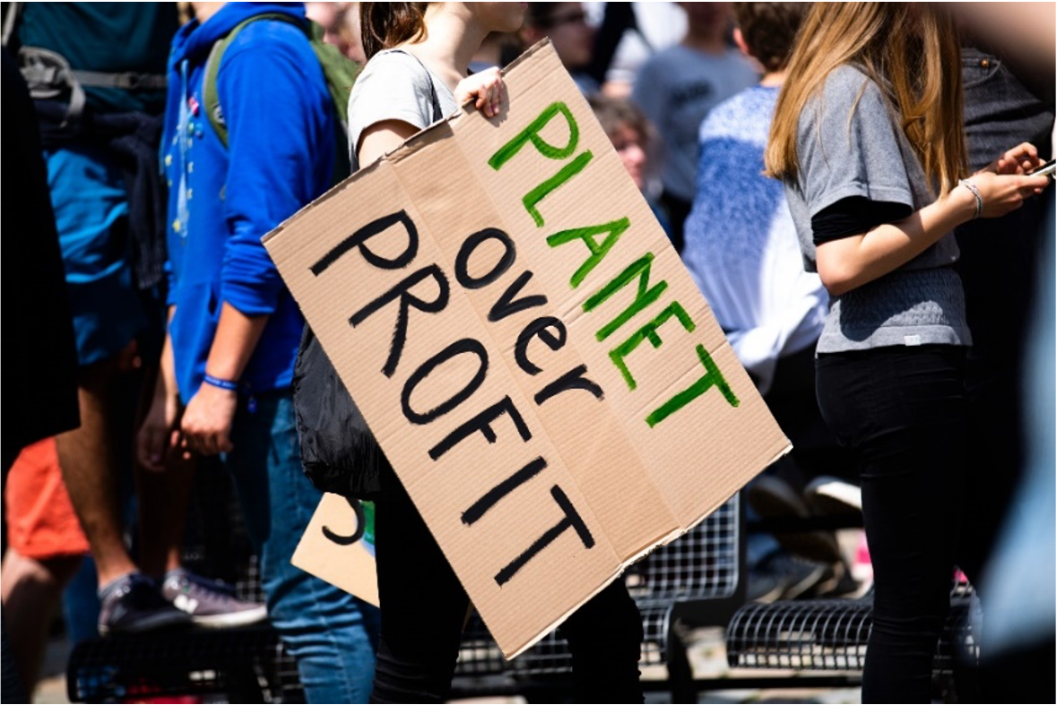 a group of people demonstrating with a sign that says “PLANET over PROFIT”.